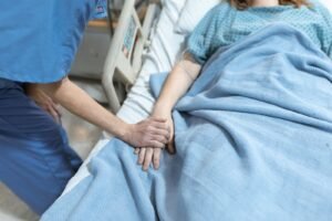 Profissional de saúde segurando a mão de um paciente em recuperação no leito hospitalar