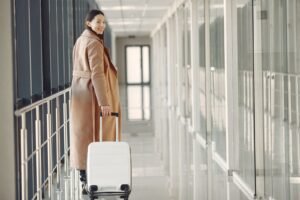 Mulher sorridente caminhando com mala de viagem em corredor de aeroporto, representando a retomada de viagens por pessoas ostomizadas