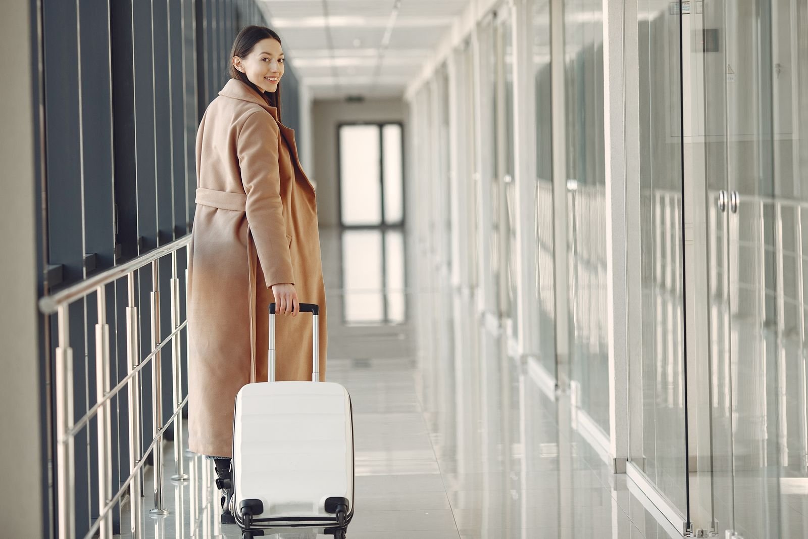 Mulher sorridente caminhando com mala de viagem em corredor de aeroporto, representando a retomada de viagens por pessoas ostomizadas