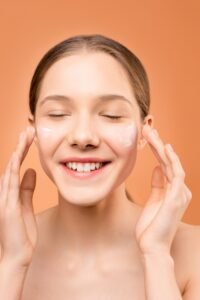 Mulher sorrindo aplicando hidratante facial com as mãos, representando cuidado com a pele seca e desidratada