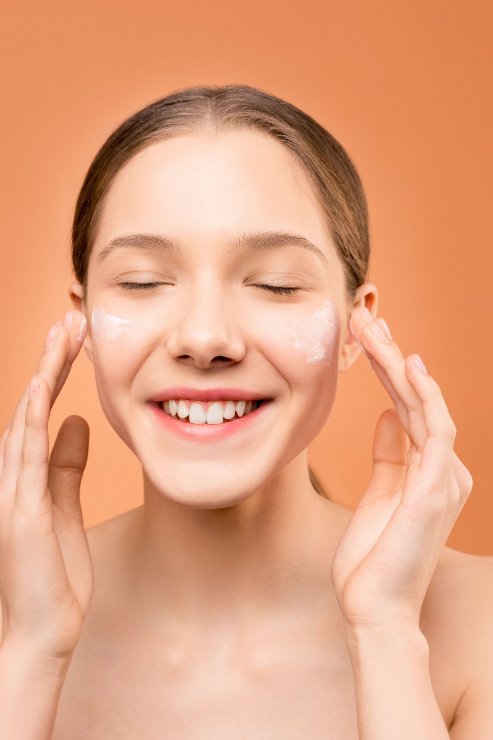 Mulher sorrindo aplicando hidratante facial com as mãos, representando cuidado com a pele seca e desidratada