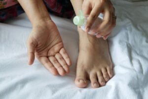 Pé e mãos recebendo hidratação com um frasco de creme, ilustrando a rotina diária de cuidados com os pés