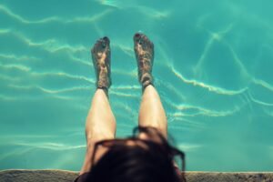 Pés descalços submersos na água de uma piscina, contexto de transmissão da verruga plantar em ambientes úmidos